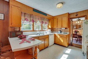Una cocina con armarios de madera, encimera blanca, una radio y una ventana con cortinas a cuadros.