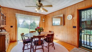 A dining area with a wooden table, four chairs, a ceiling fan, and a large window with sheer curtains. - Haysi Nature Getaway w/ Fire Pit & On-Site Creek! (Haysi)