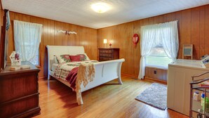 A bedroom with a wooden floor, a bed, a dresser, a washing machine, and a window with curtains. - Haysi Nature Getaway w/ Fire Pit & On-Site Creek! (Haysi)