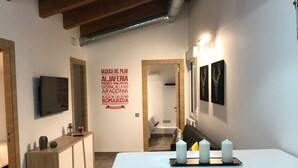 A modern dining area with a white table and two stools, a wooden console table with decorative items, and a wall with a list of names. - FLATS 20 Ático · Check-in 24h NEW!! Increíble ático en el CENTRO 1000 Estrellas! (Zaragoza)
