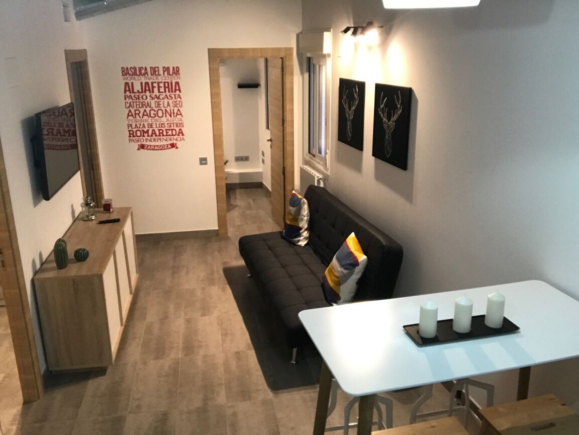 Een moderne woonkamer met een zwarte bank, een witte tafel met kaarsen en een wand met decoratieve plaquettes.