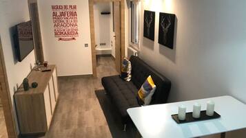 Een moderne woonkamer met een zwarte bank, een witte tafel met kaarsen en een wand met decoratieve plaquettes.