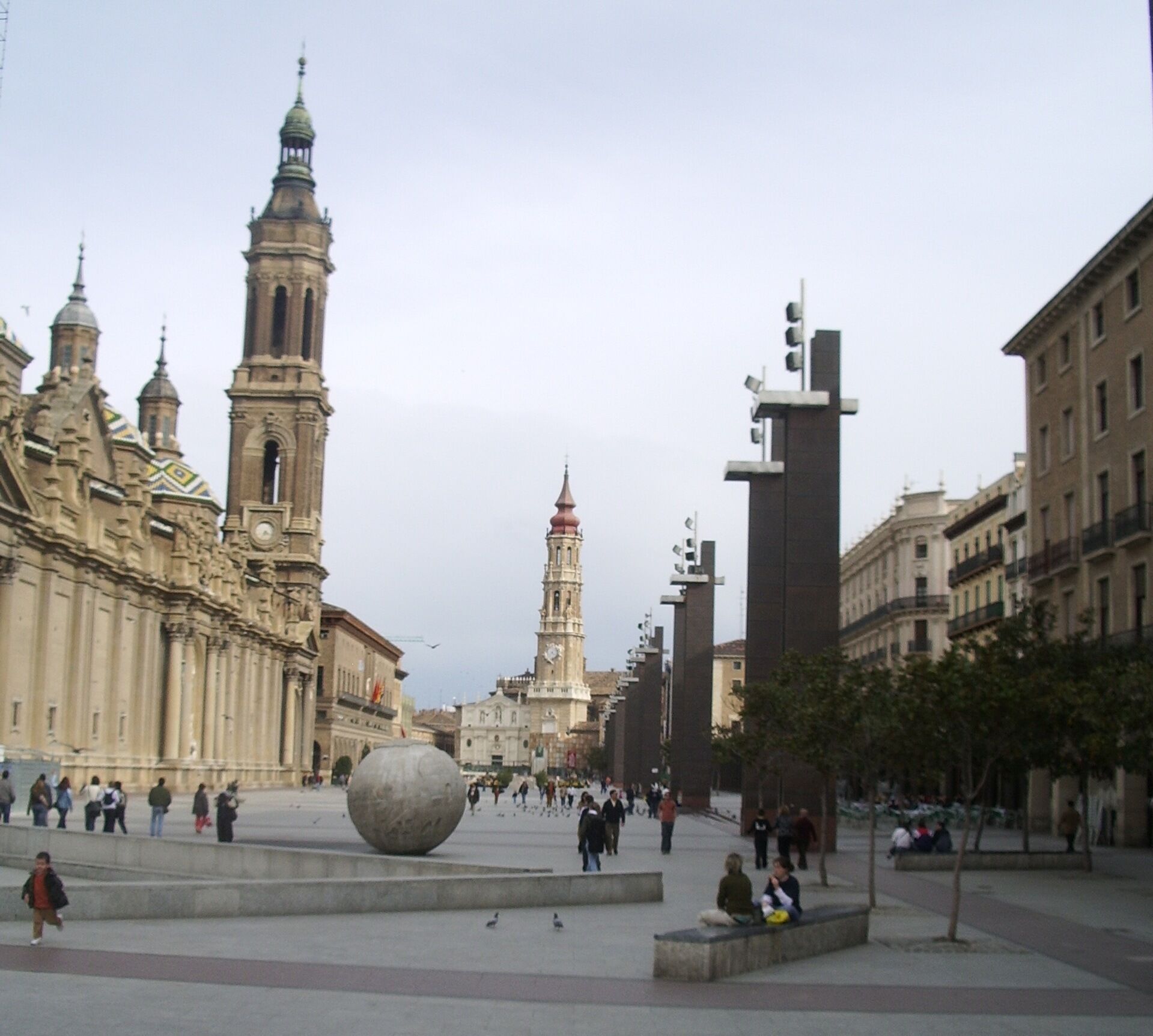 Una plaza pública con edificios históricos, una destacada torre del reloj y una gran escultura esférica.