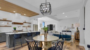 A modern kitchen with a central island, bar stools, and a dining table with chairs. - Luxury Downtown Loft -Walk to Dining-Near Campbell & Ft. Bragg (Lillington)