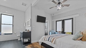 A modern bedroom with a large bed, a ceiling fan, a TV, and a view of the outdoors. - Luxury Downtown Loft -Walk to Dining-Near Campbell & Ft. Bragg (Lillington)
