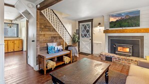 Un salon avec une cheminée, un escalier en bois et une grande fenêtre.