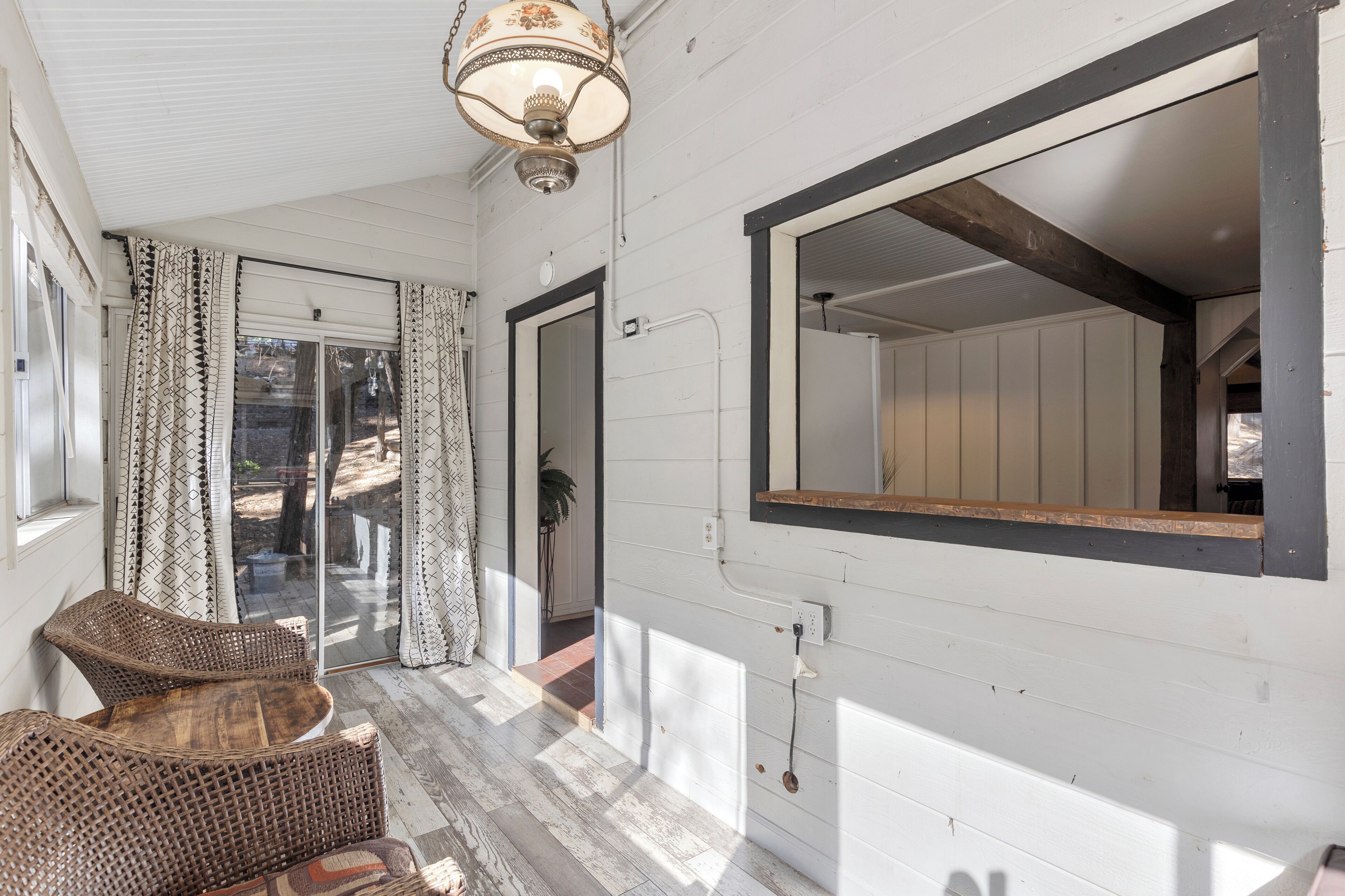 A covered porch with wicker furniture, a large mirror, and a ceiling light fixture.
