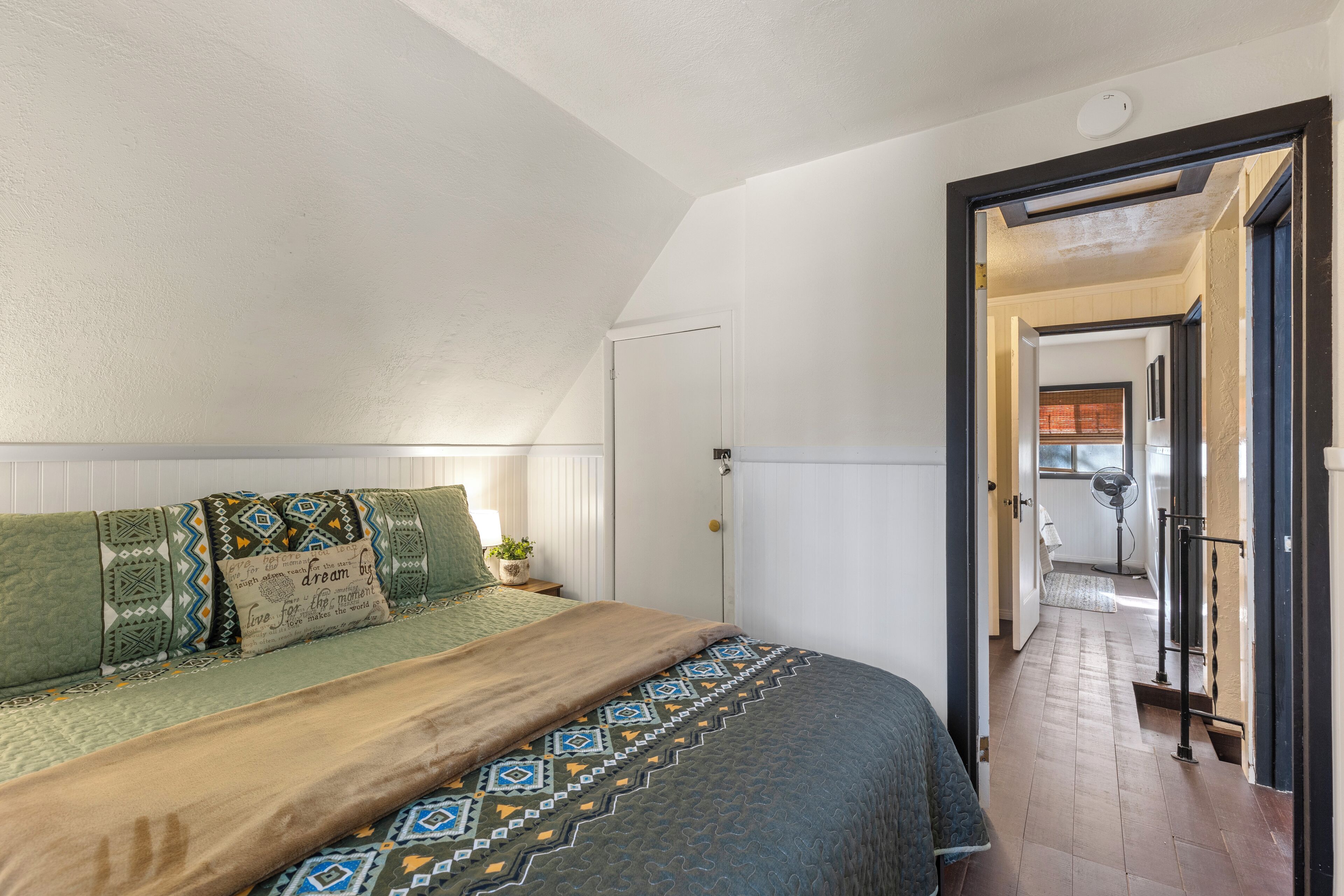 A bedroom with a bed, pillows, a bedside table, and a window.