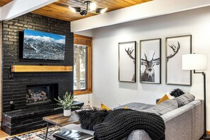 A living room with a fireplace, a television, and three framed deer antlers on the wall. - Motherlode A5 (Breckenridge)