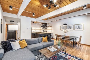 Ein modernes Wohnzimmer mit einem grauen Sofa, einem Holztisch und einem Essbereich mit Tisch und Stühlen.