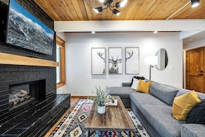 A living room with a fireplace, a gray sofa, a coffee table with a plant, and three deer wall art pieces.