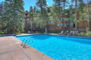 Une piscine à l’eau d’un bleu cristallin, entourée de chaises longues et d’une terrasse en bois.