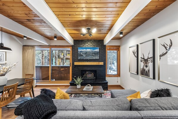 A living room with a fireplace, a sofa, a coffee table, and a view of the outdoors. - Motherlode A5 (Breckenridge)