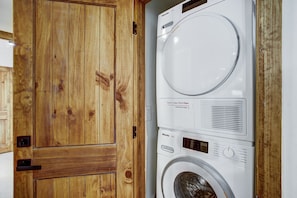 Un appareil combiné lave-linge et sèche-linge, de type « superposé », doté d’une porte en bois.