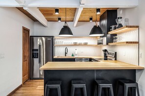 Une cuisine moderne dotée d’un îlot central, d’appareils électroménagers en acier inoxydable, d’éléments décoratifs en bois et de luminaires suspendus.