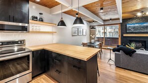 A modern kitchen with a wooden island, stainless steel appliances, pendant lighting, and a dining area with a fireplace. - Motherlode A5 (Breckenridge)