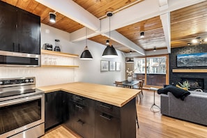A modern kitchen with a wooden island, stainless steel appliances, pendant lighting, and a dining area with a fireplace.