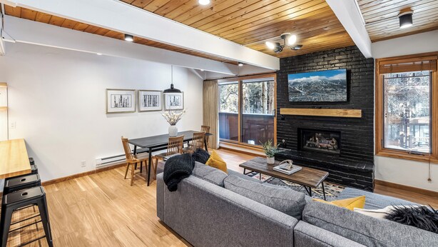 A modern living room with a fireplace, wooden ceiling, and large windows. - Motherlode A5 (Breckenridge)