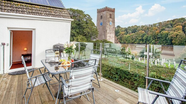 A balcony with a table, chairs, and a view of a tower and forest. - 5 bedroom accommodation in Stoke Gabriel, near Totnes (Stoke Gabriel, near Totnes)