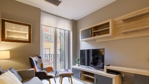 Ein modernes Wohnzimmer mit einem grauen Sofa, einem kleinen Tisch und einem Fernseher.