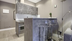 Eine moderne Küche mit grauen Schränken, einem eingebauten Backofen und einer Bar mit zwei klaren Hockern.