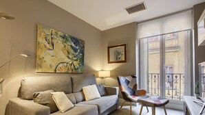 Ein Wohnzimmer mit einer Couch, einem Sessel, einem Gemälde und einem Balkon mit Geländer.