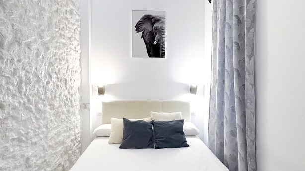 Uma cama bem arrumada com lençóis brancos e toalhas dobradas, uma cabeceira e um quadro com uma imagem de elefante na parede.