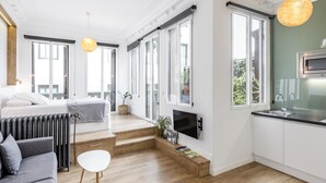 A modern apartment with a living room, kitchen, and dining area. It features large windows, a fireplace, and a flat-screen TV. - Home Suite Home I - Studio apartment with terrace in the center (Madrid)