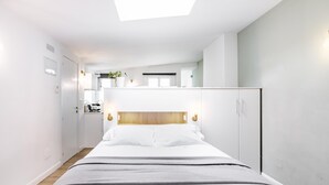 A modern bedroom with a bed, a skylight, and a kitchenette in the background. - Home Suite Home II - Studio apartment with large shared terrace (Madrid)