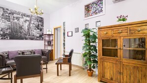 Un salon décoré d’une œuvre d’art murale représentant un paysage urbain en noir et blanc, d’un lustre, d’un meuble en bois aux portes vitrées et d’une plante en pot.