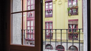 Vue depuis un balcon avec une porte en bois, donnant sur un bâtiment jaune avec des volets rouges et de nombreuses fenêtres ornées de balcons en fer forgé.