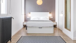 A modern bedroom with a large bed, bedside lamps, a hanging light fixture, and a patterned rug. - Home Suite Home III - Studio apartment with large shared terrace (Madrid)