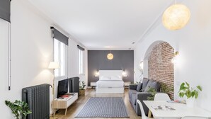 A modern, compact hotel room with a bed, a sofa, a dining table, and a TV. - Home Suite Home IV - Studio apartment with large shared terrace (Madrid)