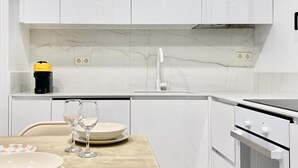 A modern kitchen with white cabinets, a marble backsplash, a built-in oven, and a coffee maker on the countertop. - Puerta de Toledo VII - 2-Bedroom Apartment (Madrid)
