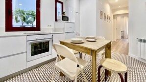 A modern kitchen with white cabinetry, a built-in oven, and a dining area with a wooden table and white chairs. - Puerta de Toledo VII - 2-Bedroom Apartment (Madrid)