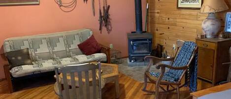 A cozy room with a sofa, a rocking chair, a wooden table, a lamp, and a fireplace.