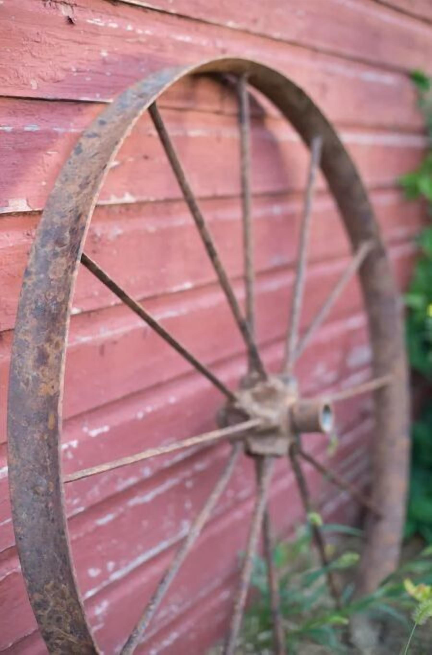 Primer plano de una rueda de metal oxidada contra una pared de madera roja.