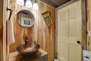 A wooden bathroom with a large vessel sink, a round mirror, and a door with a light switch. - Rustic Caledonia Cabin Near State Parks & Boating! (Caledonia)