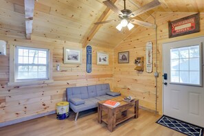 A cozy room with wooden walls, a gray sofa, a wooden coffee table, and a ceiling fan. - Rustic Caledonia Cabin Near State Parks & Boating! (Caledonia)