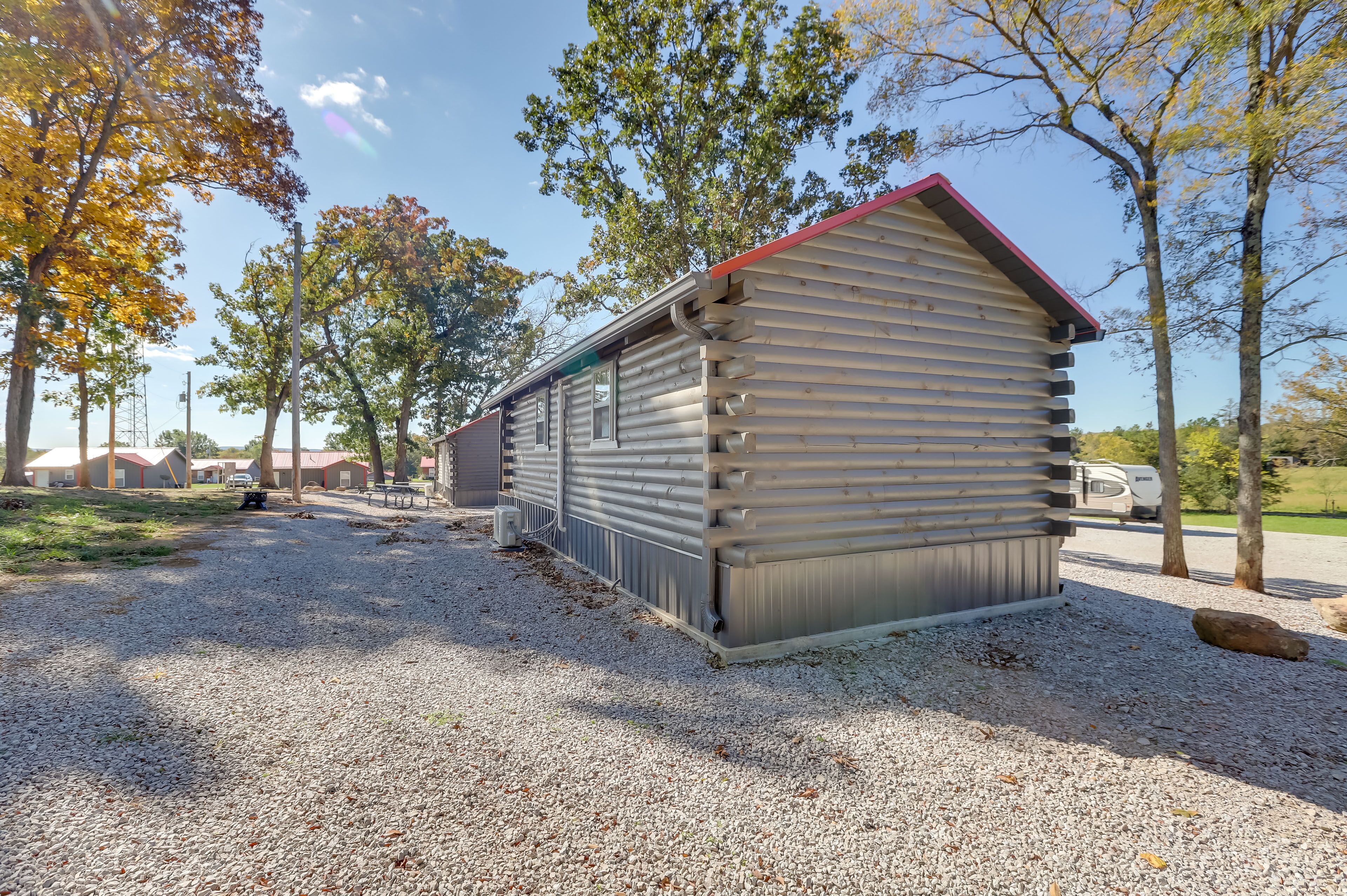 A small, single-story cabin with a red roof, surrounded by gravel and trees.
