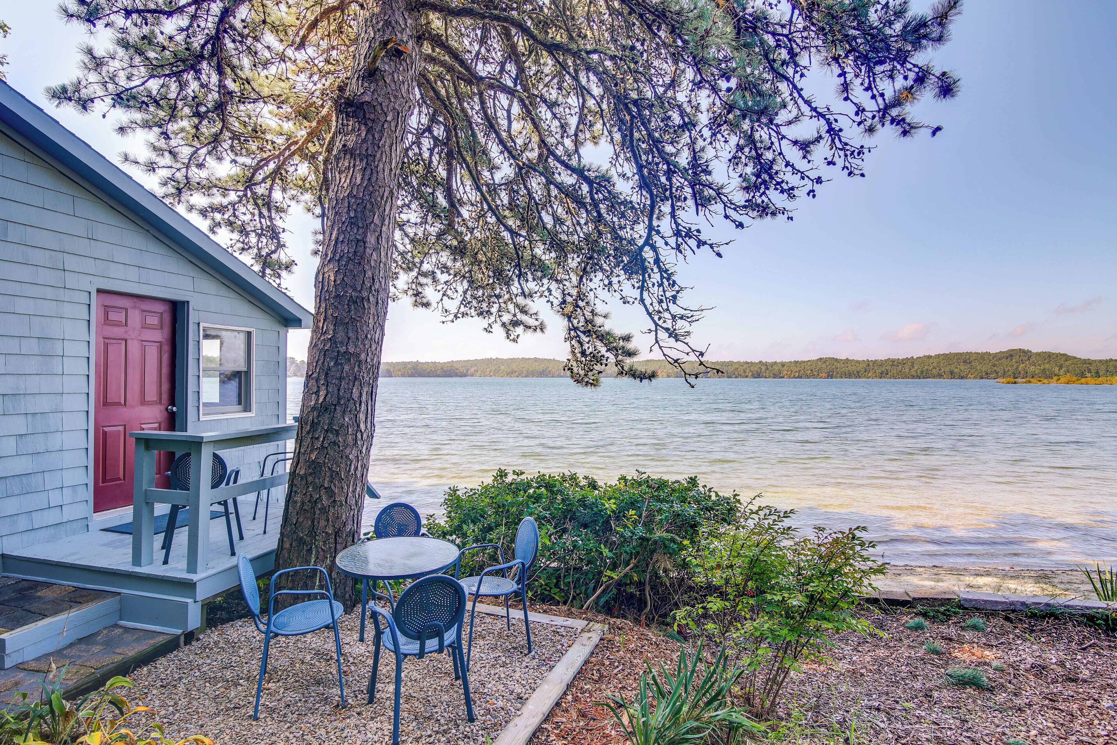 Una cabaña junto al lago con terraza, asientos exteriores y vistas al lago.