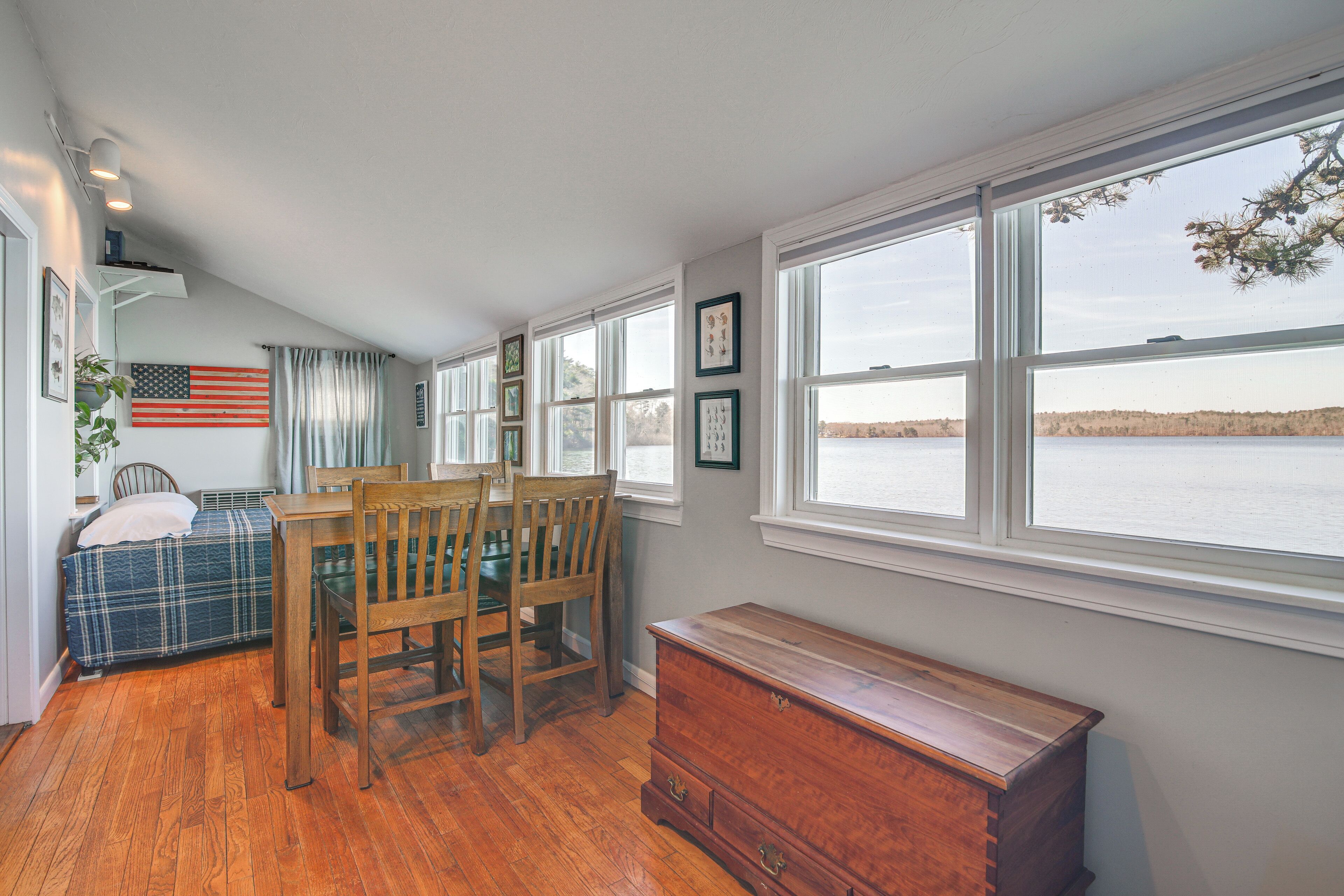 A room with a bed, a table with chairs, a dresser, and large windows overlooking a body of water.