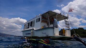 Un bote con camarote y escalera, flotando sobre agua bajo un cielo despejado y nublado.