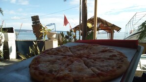 A pizza on a tray with a view of the sea and a small structure in the background.