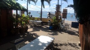 Un espacio al aire libre con mesas y sillas, plantas en macetas y vistas al mar con barcos.
