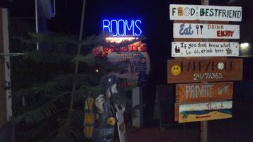 Un cartel con varios letreros que incluyen 'HABITACIONES', 'Food is Bestfriend', 'Comer, beber y disfrutar', 'Si no sabes qué hacer, bebe cerveza', 'Hora feliz las 24 horas, los 7 días de la semana, los 365 días del año', y 'Señal privada'.