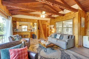 A cozy cabin interior with a living room, wooden walls, a ceiling fan, and a kitchen area.