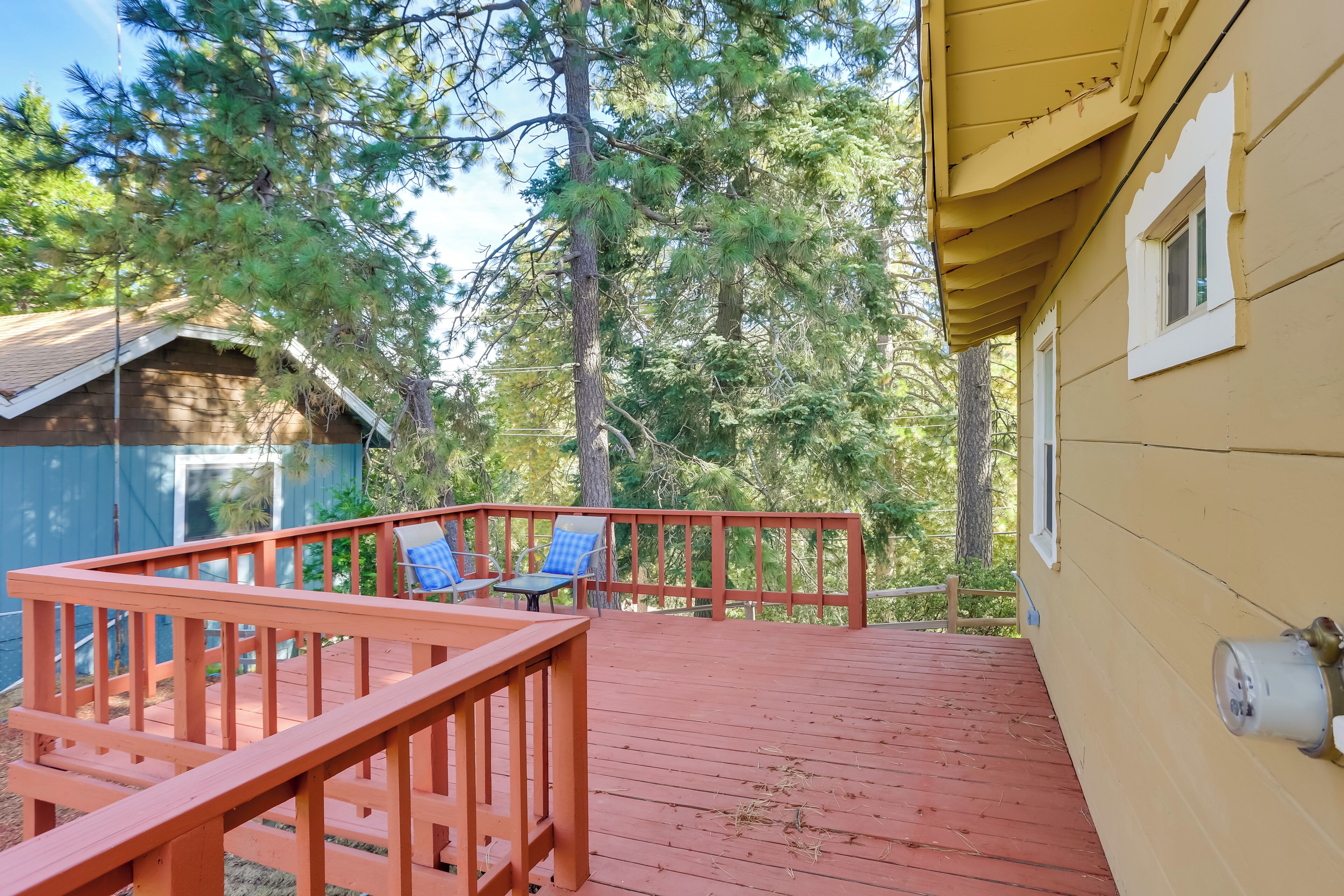 A wooden deck with a railing, two blue chairs, and a table.