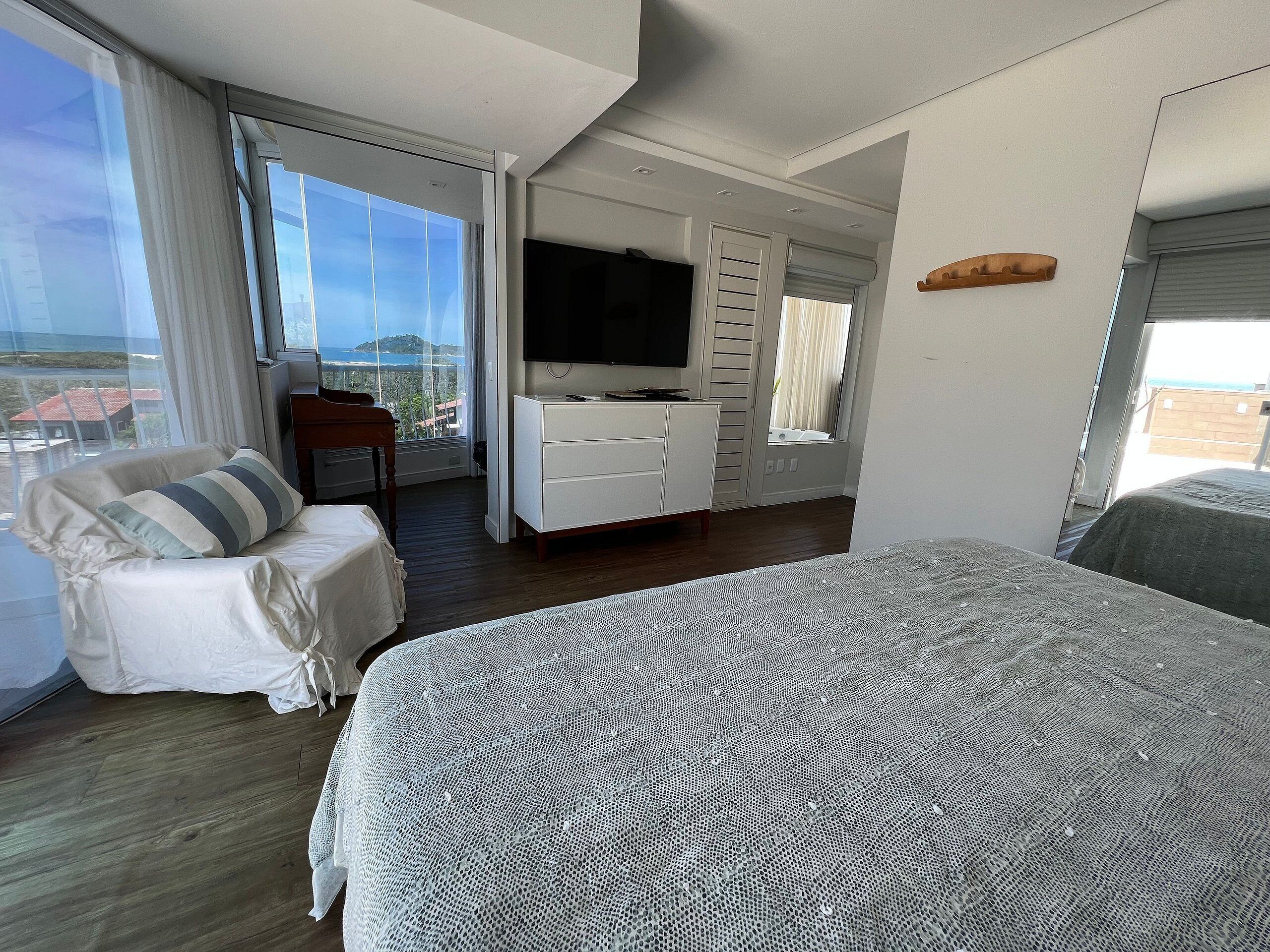 A modern bedroom with a large bed, a TV, a seating area, and a balcony with a view.