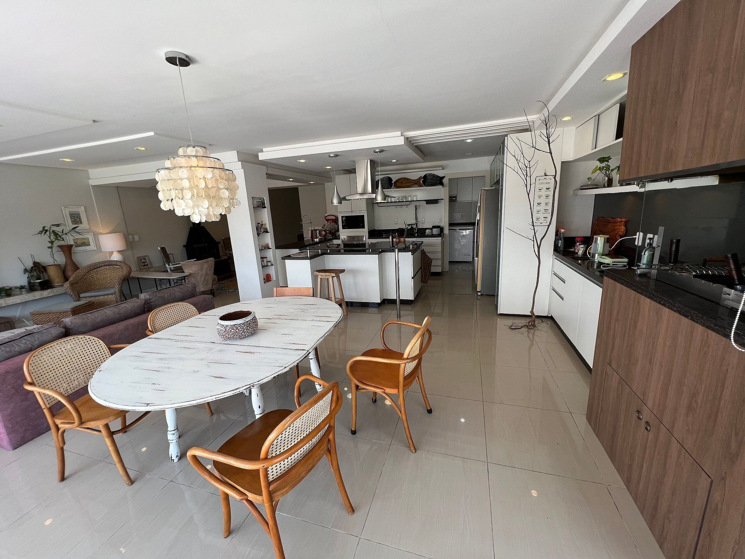 A modern kitchen with white cabinets, a central island, and a dining area with a round table and wicker chairs.